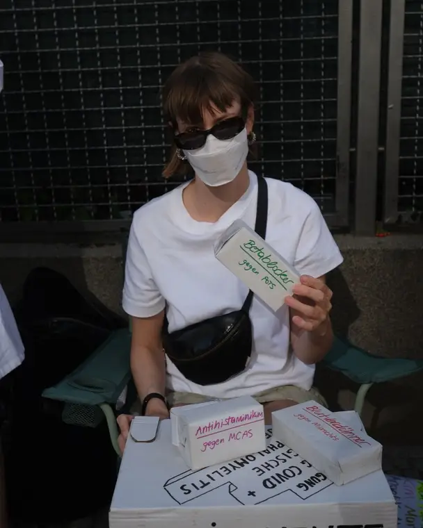 Person in sunglasses and a mask holding up a medicine box labelled beta blockers