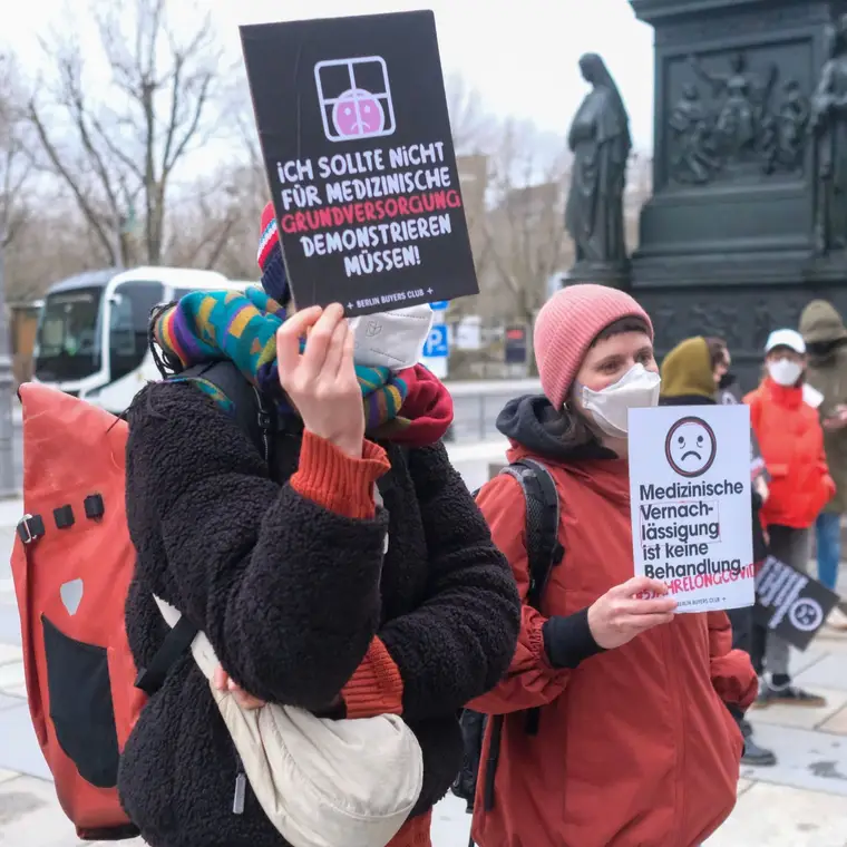 Protesters in masks holding signs about basic medical care for Long Covid and ME/CFS