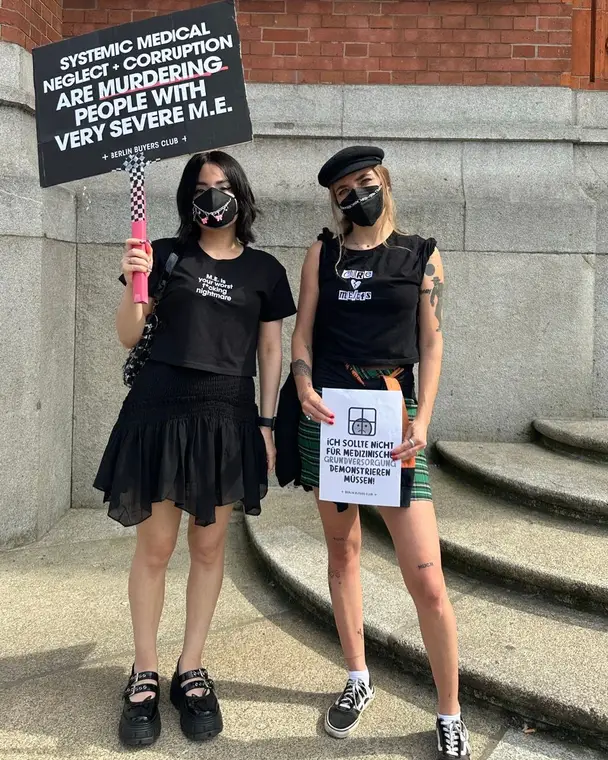 Two activists in masks with signs outside the Rotes Rathaus at a #LiegendDemo for severe ME